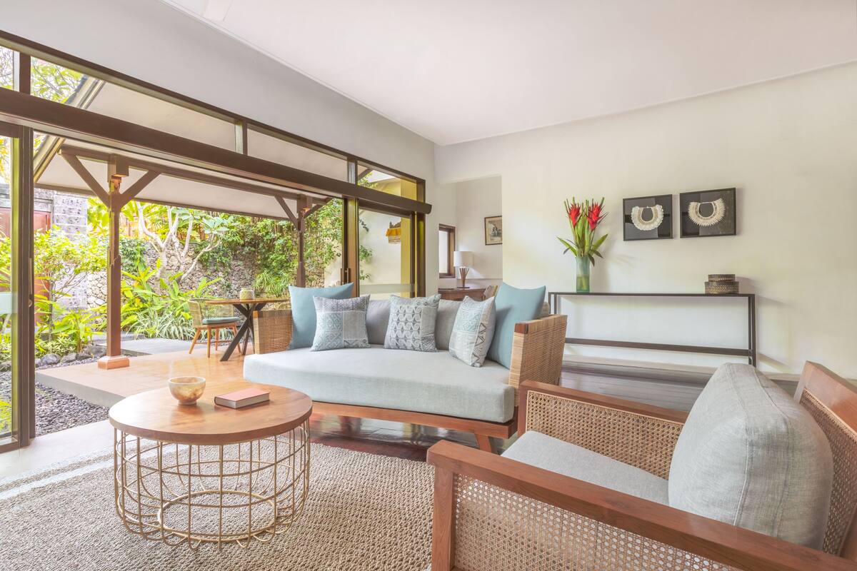 A spacious living area with a sofa, chairs, and a coffee table. There is a large window providing a view of the outdoors.