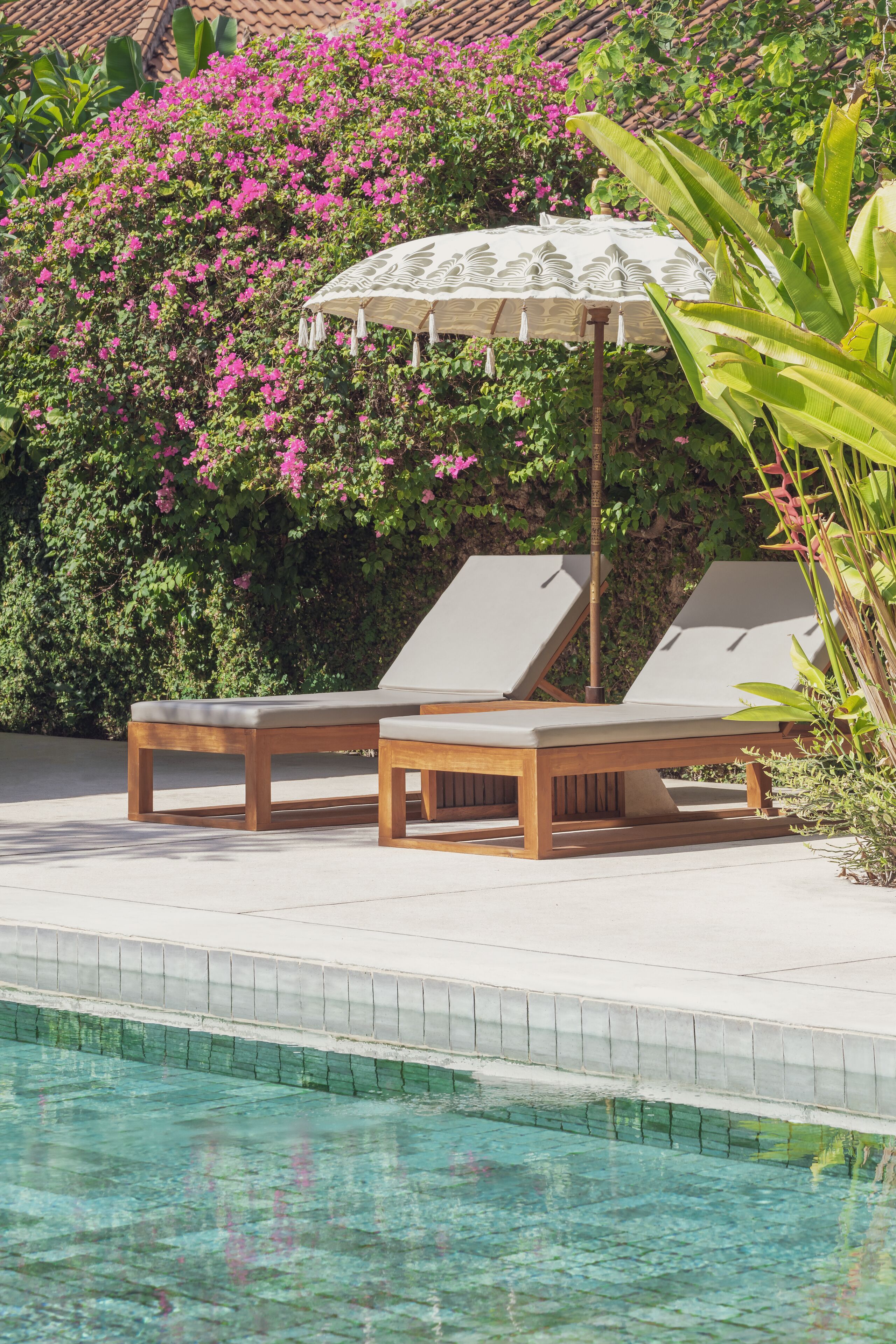 Un área junto a la piscina con dos sillas reclinables y una mesa bajo una sombrilla.