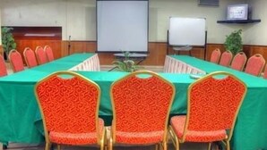 Une salle de conférence avec une longue table, des chaises à motifs rouges, un tableau blanc et un écran de projection.