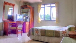 Une chambre à coucher avec un lit, un bureau avec une chaise, une télévision et une fenêtre avec des rideaux.