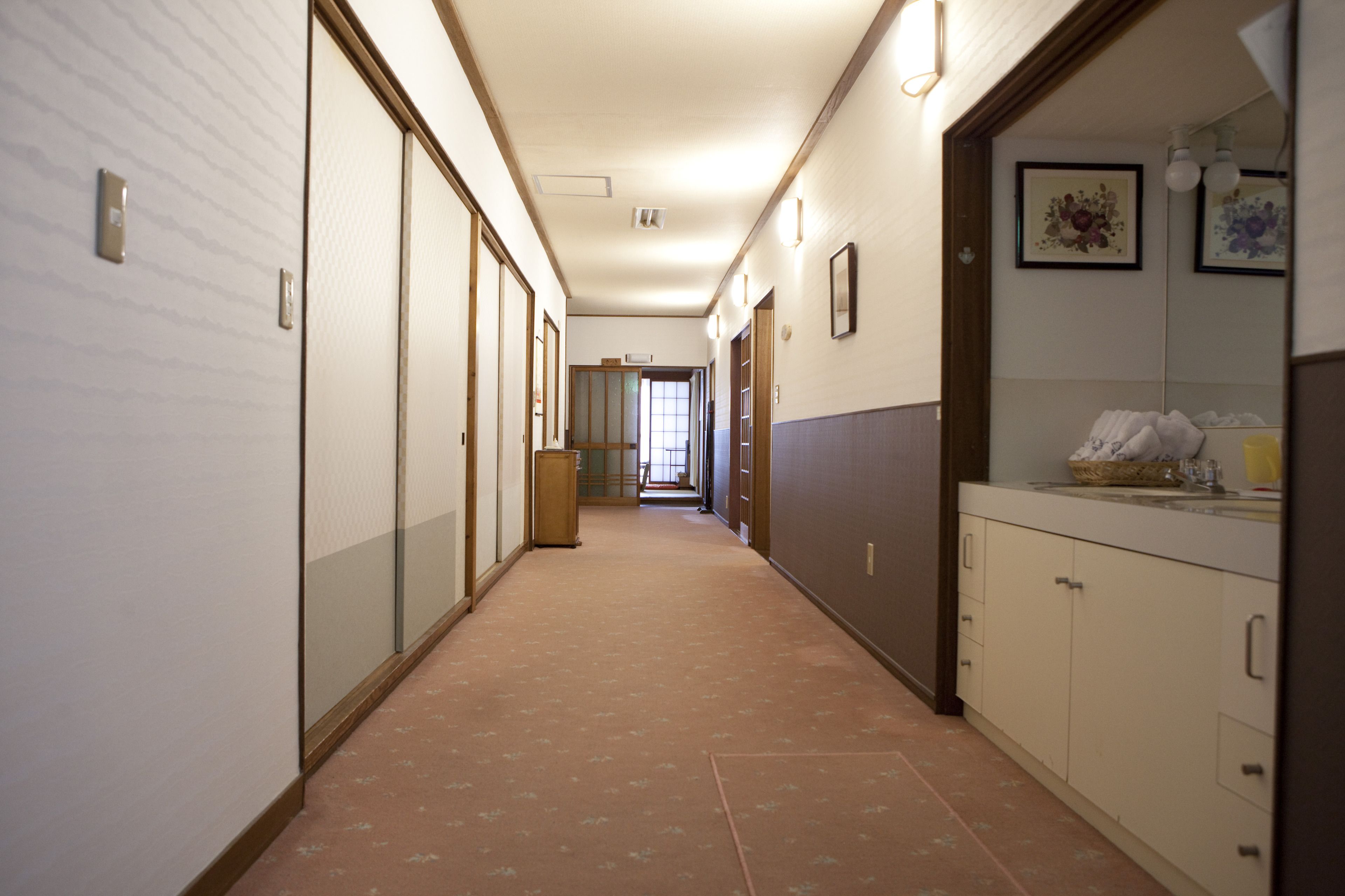 Un couloir d’hôtel avec un sol recouvert de moquette, des portes en bois et un coin cuisine équipé de placards et d’un évier.