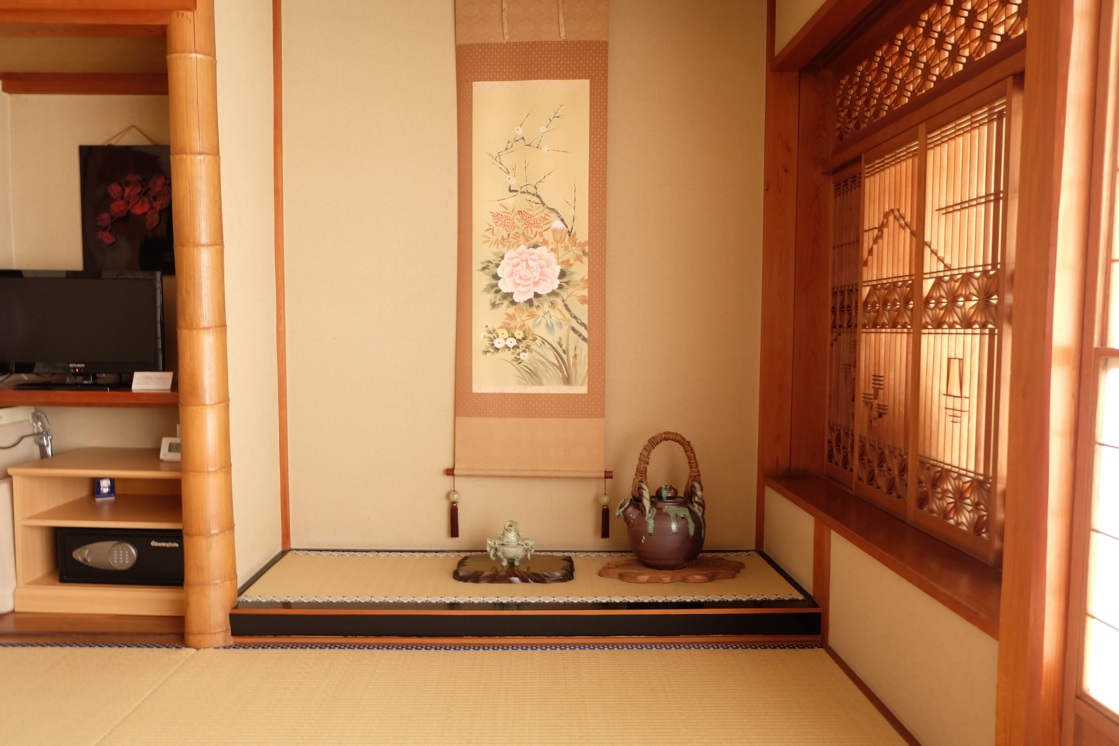 Una habitación japonesa tradicional con suelo de tatami, una pantalla shoji, un pergamino de caligraf ía colgado en la pared, una rana de cerámica y un juego de té.