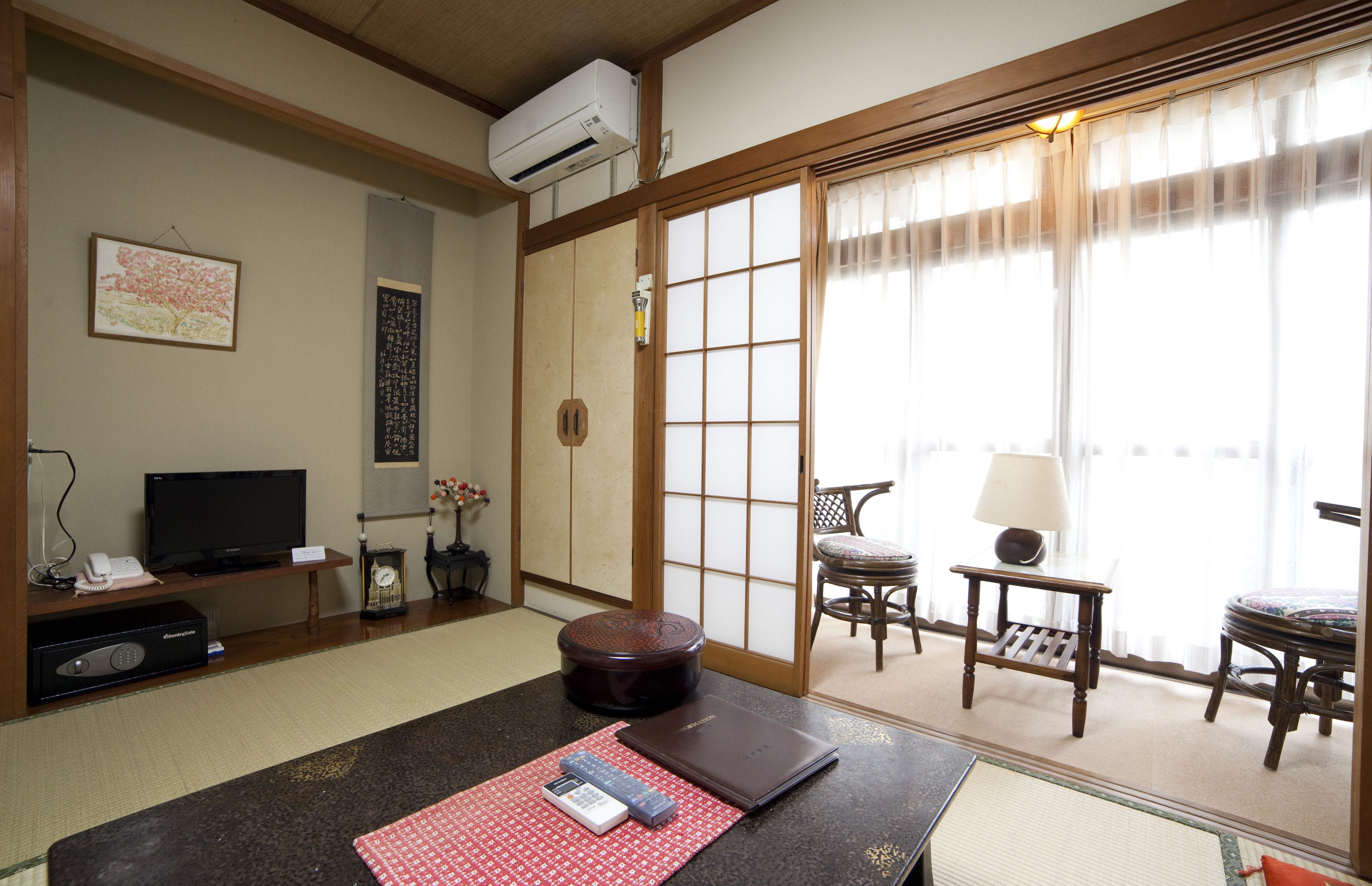 A traditional Japanese room with tatami flooring, a television, a futon, and sliding doors leading to a balcony.