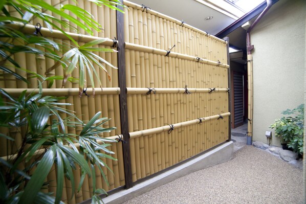 A bamboo fence with a wooden door, a gravel pathway, and potted plants. - Hinodeya Ryokan (Ito)
