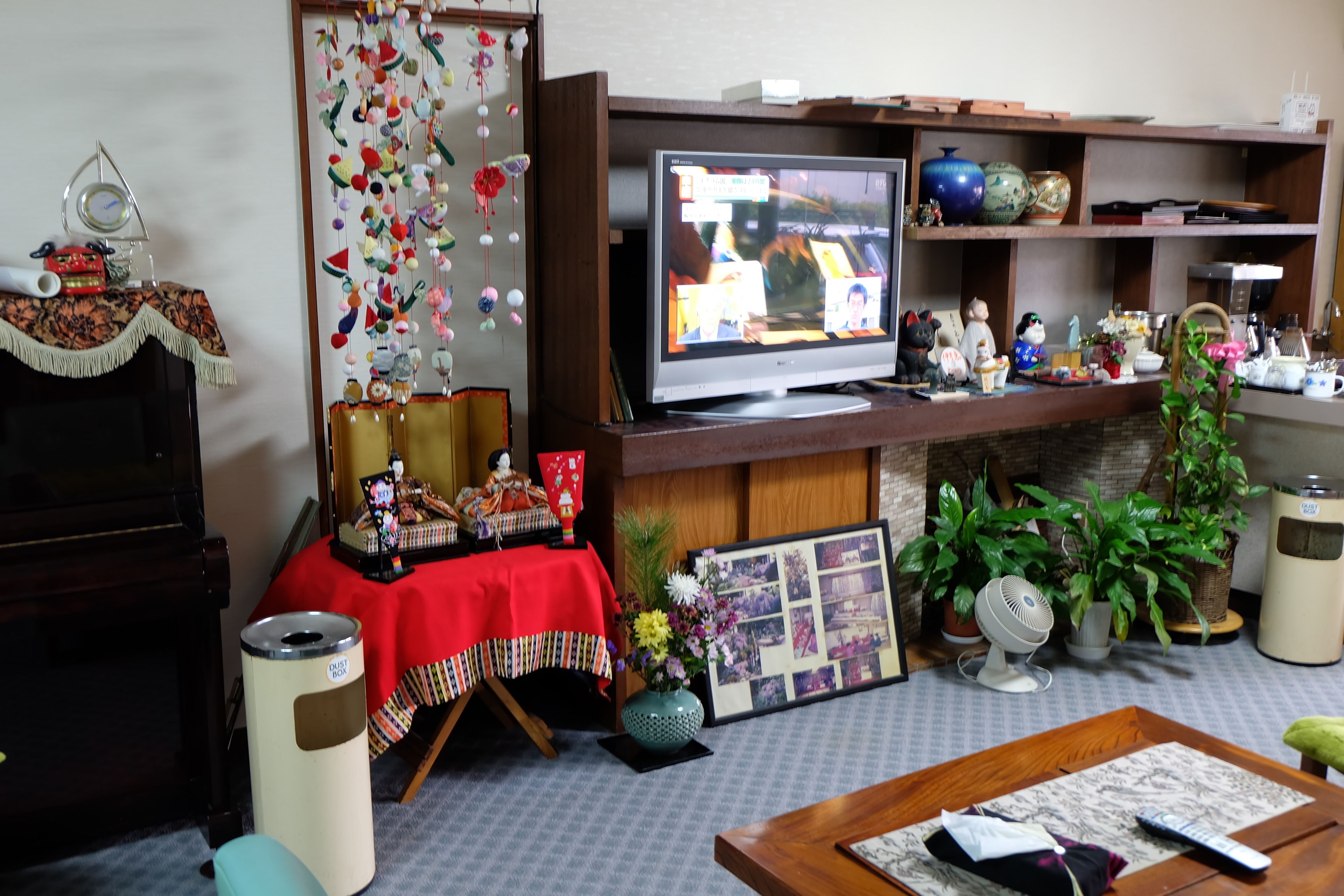 Ein Wohnzimmer mit Fernseher, Klavier, einem Tisch mit roter Tischdecke und verschiedenen Dekorationselementen.