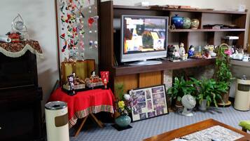 Ein Wohnzimmer mit Fernseher, Klavier, einem Tisch mit roter Tischdecke und verschiedenen Dekorationselementen.