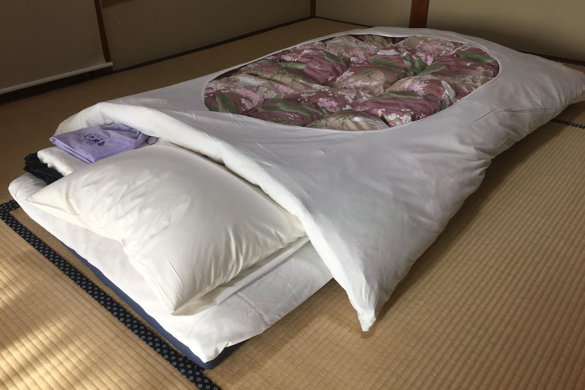 Une pièce avec un sol recouvert de tatamis, comprenant un lit, des oreillers et une couverture.