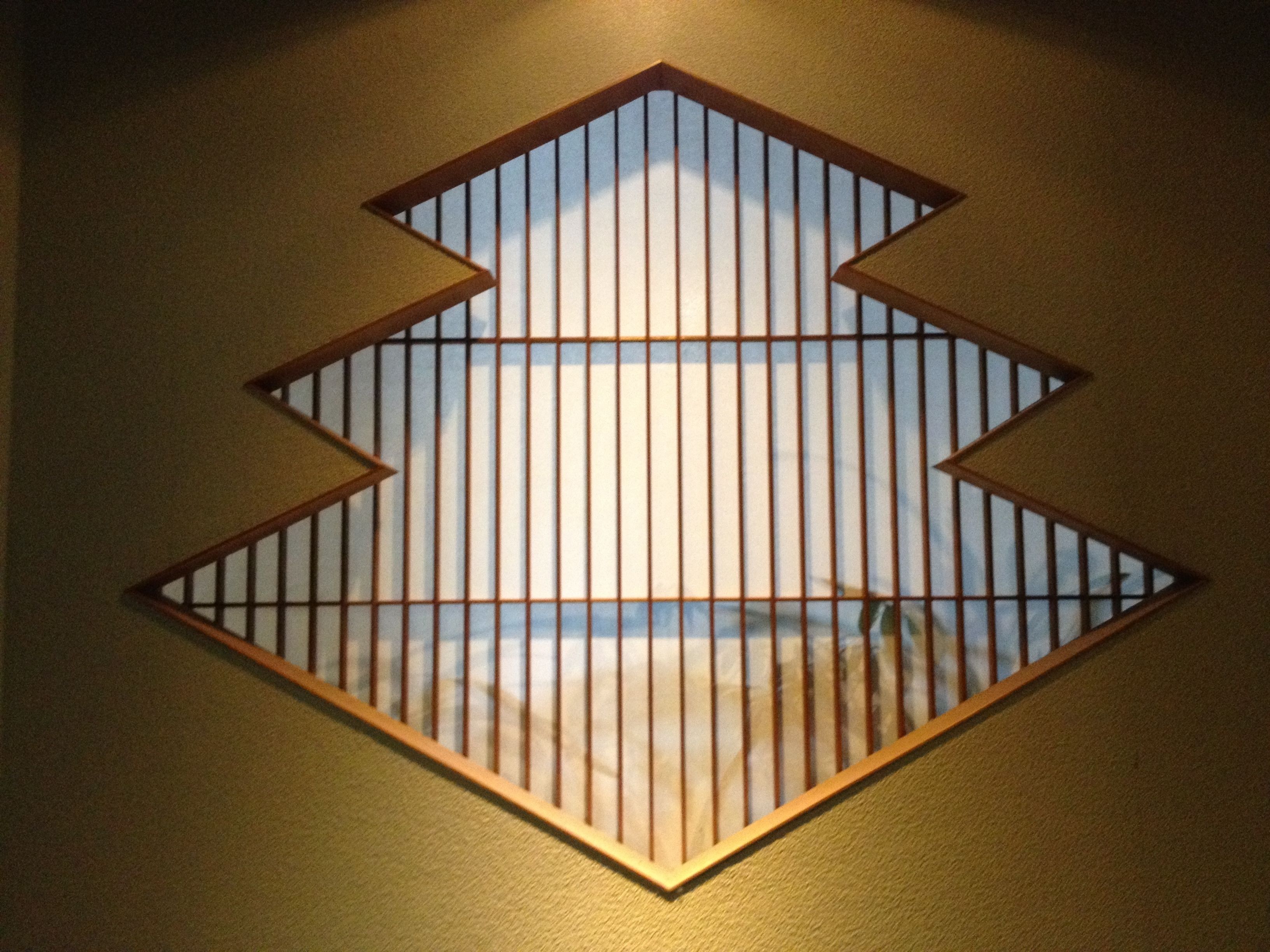 Een geometrisch wandontwerp met een diamantvormig uitsparing dat een strandscène onthult.