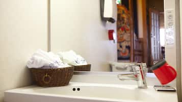 A bathroom sink with a basket of towels, a red cup, and a mirror reflecting a colorful painting.