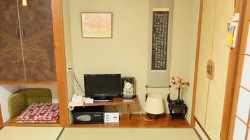 A traditional Japanese room with tatami flooring, a futon bed, a television, a clock, a lamp, and a calligraphy scroll.