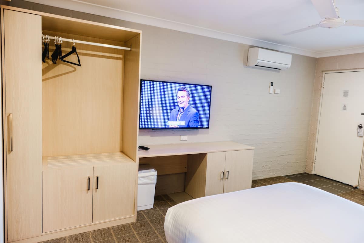 A hotel room with a bed, a TV on a stand, a wardrobe, and a trash bin.