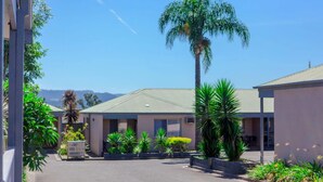 A motel with a central parking area, surrounded by various plants and a palm tree. - Balan Village Motel (Bomaderry)