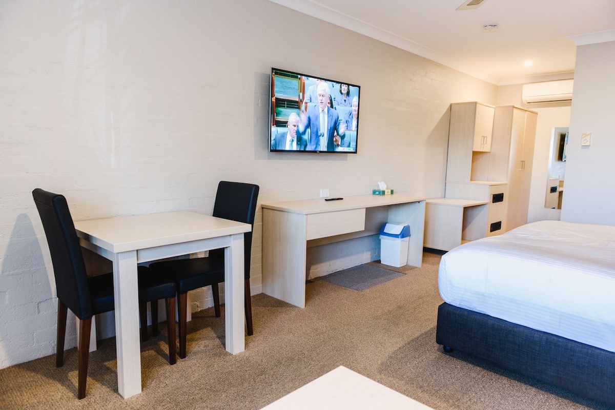 A hotel room with a bed, a desk, and a TV mounted on the wall.
