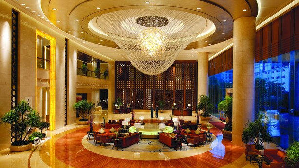 A spacious lobby with a large chandelier, multiple seating areas, and a view of the city through large windows. - HJ International Hotel (Dongguan)