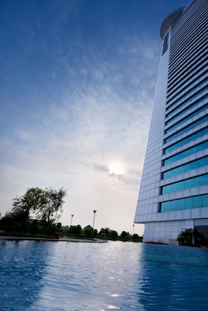 A modern building with a reflective glass facade, a clear sky, and a calm pool area.