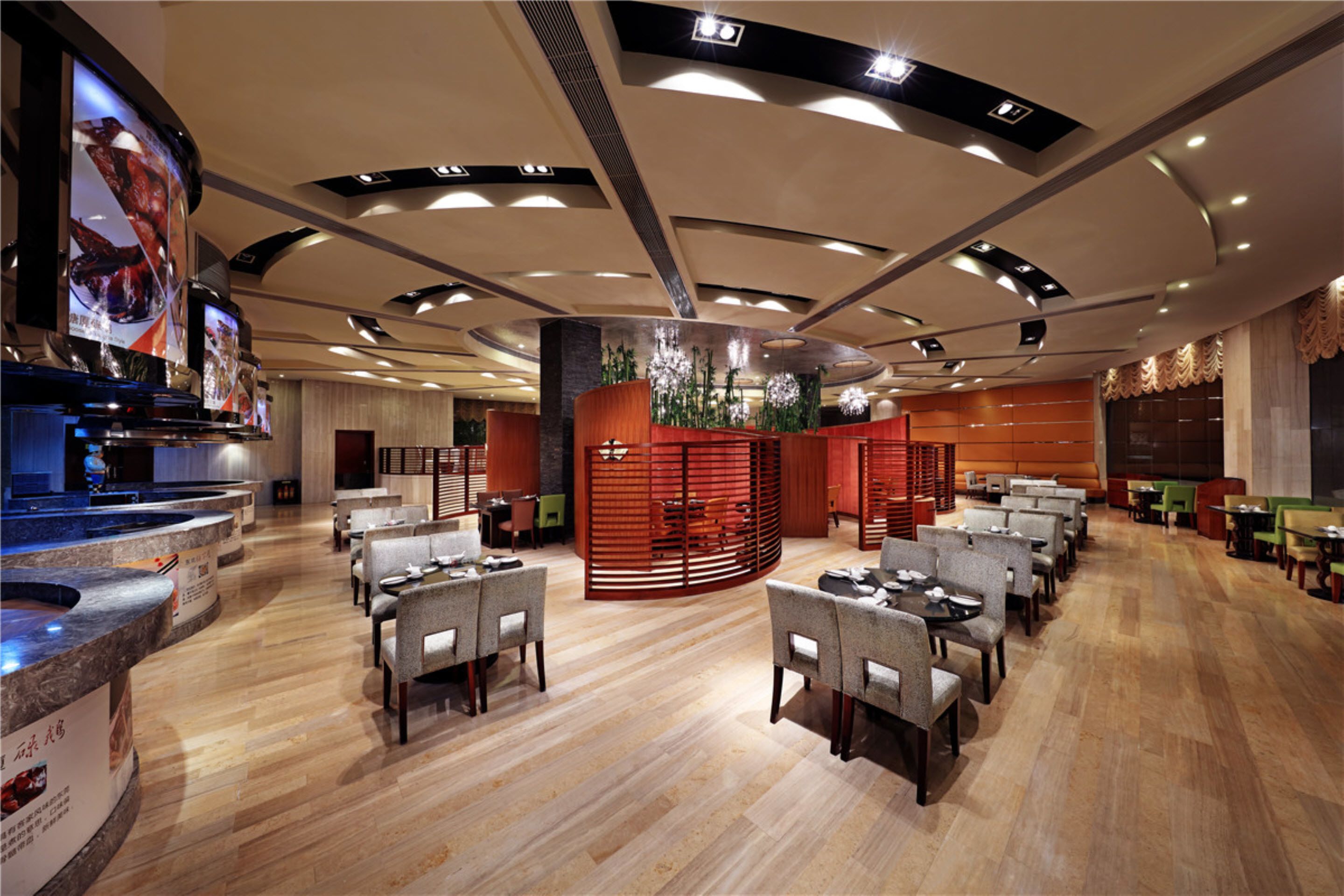 A modern restaurant with a central seating area, a bar with a large screen, and a wooden floor.