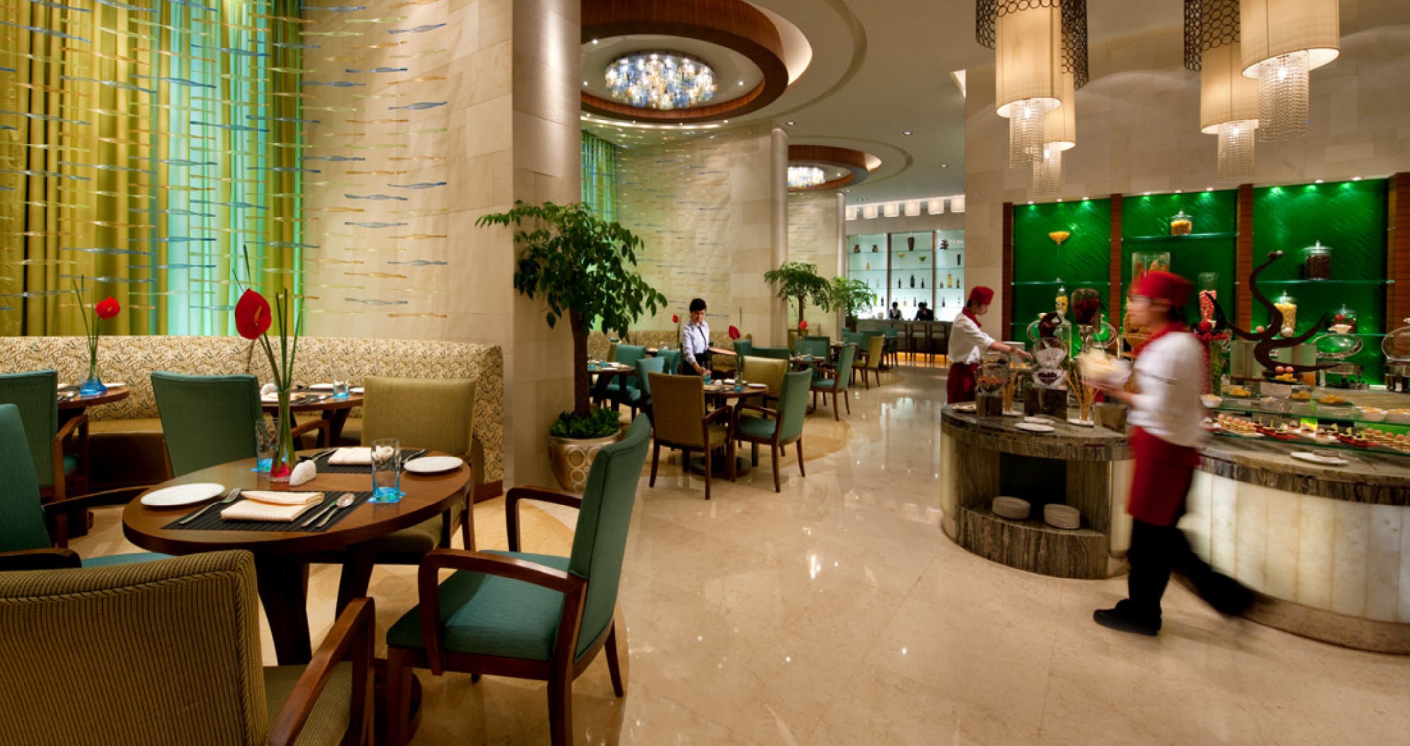 Un vestíbulo de hotel con una barra central, zonas de estar y una planta grande.