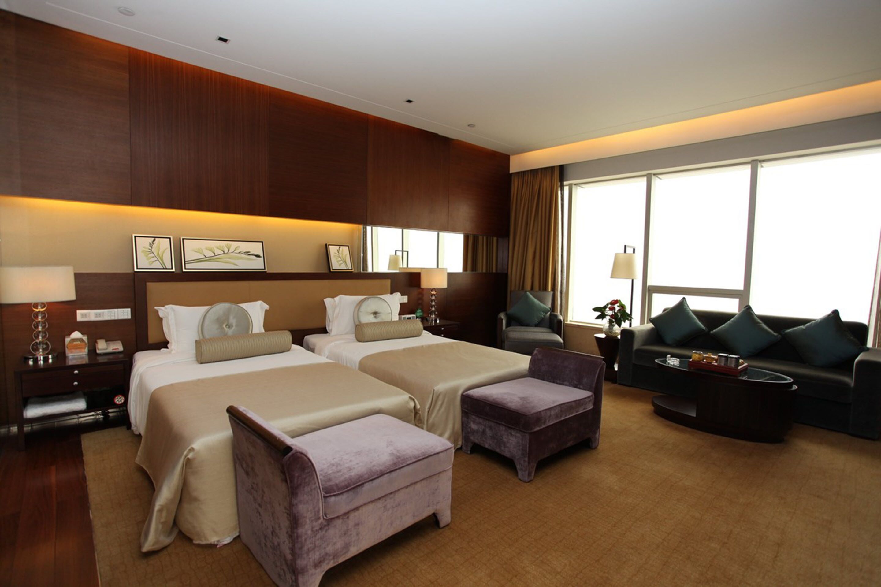 A hotel room with two beds, a sofa, a coffee table, and a large window.