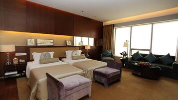 A hotel room with two beds, a sofa, a coffee table, and a large window.