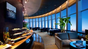 A modern hotel lobby with a curved reception desk, a seating area with sofas, and large windows offering a city view. - HJ International Hotel (Dongguan)