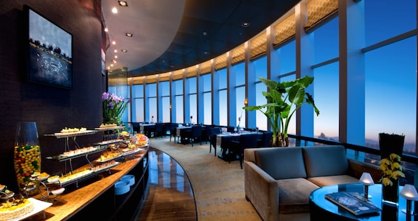 A modern hotel lobby with a curved reception desk, a seating area with sofas, and large windows offering a city view.