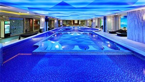 A large indoor swimming pool with a blue-tiled floor and ceiling, surrounded by seating areas and a reception desk. - HJ International Hotel (Dongguan)