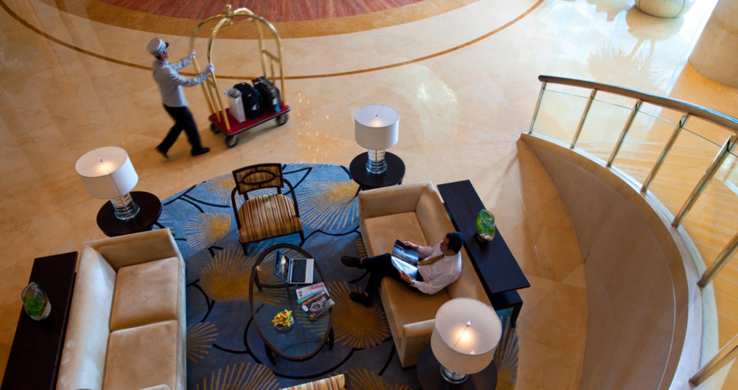 A spacious lobby with a central seating area, a luggage cart, and a person walking.