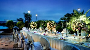 An outdoor dining area with tables set for a formal event, surrounded by palm trees and decorative lighting. - HJ International Hotel (Dongguan)