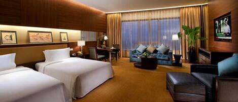 A hotel room with two beds, a sofa, a coffee table, and a TV.
