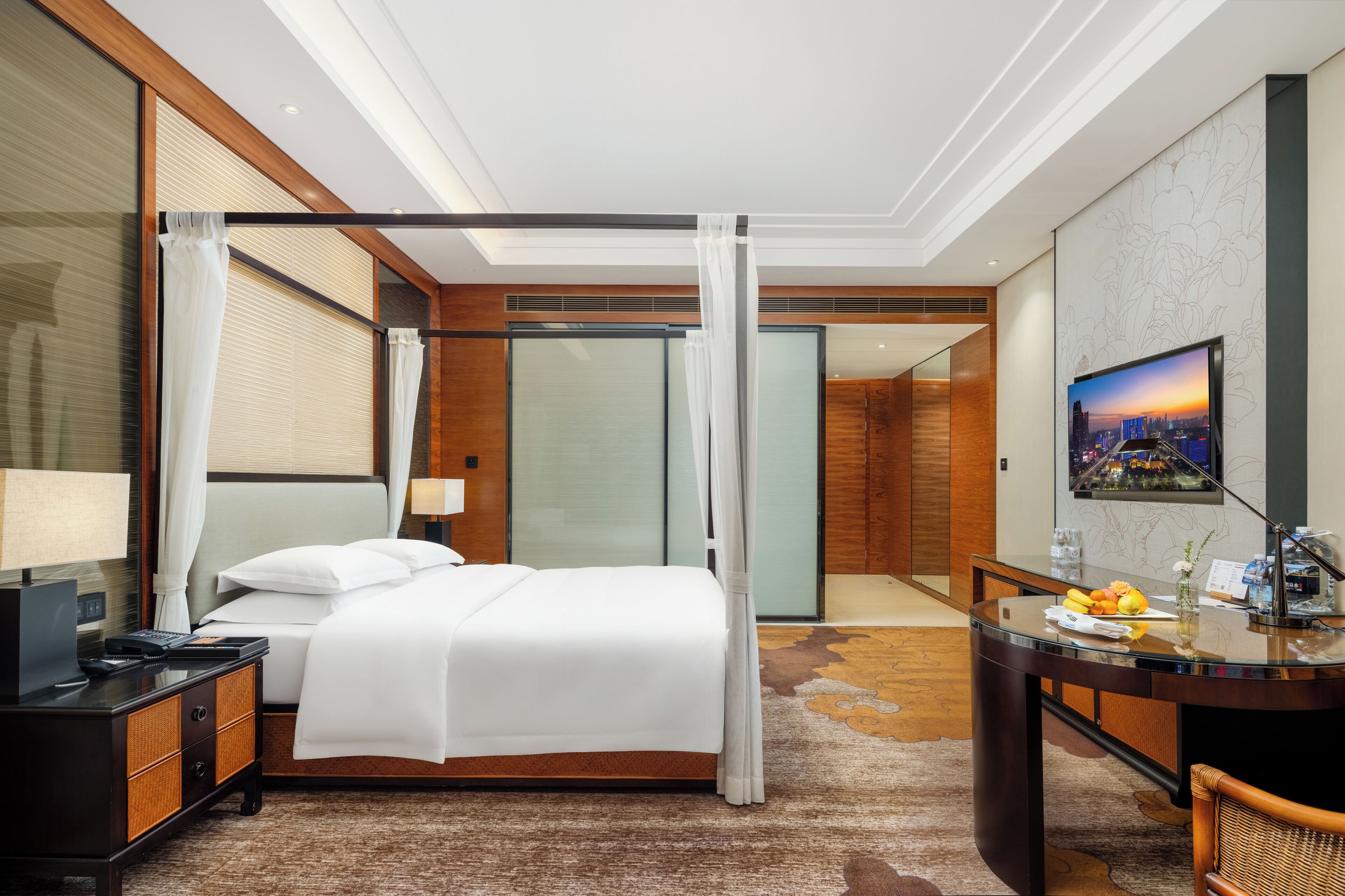 Een moderne hotelkamer met een bed, nachtkastje, bureau en een groot raam.