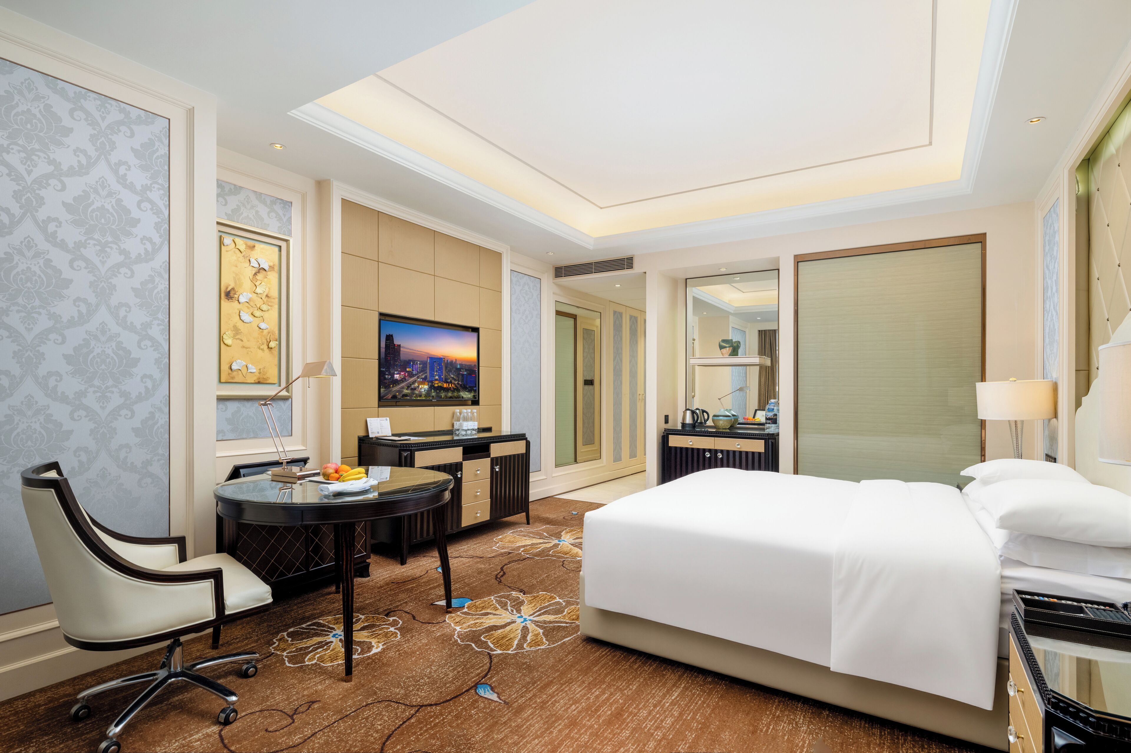 A hotel room with a large bed, a desk with a chair, a television, and a dining area with a table and chairs.