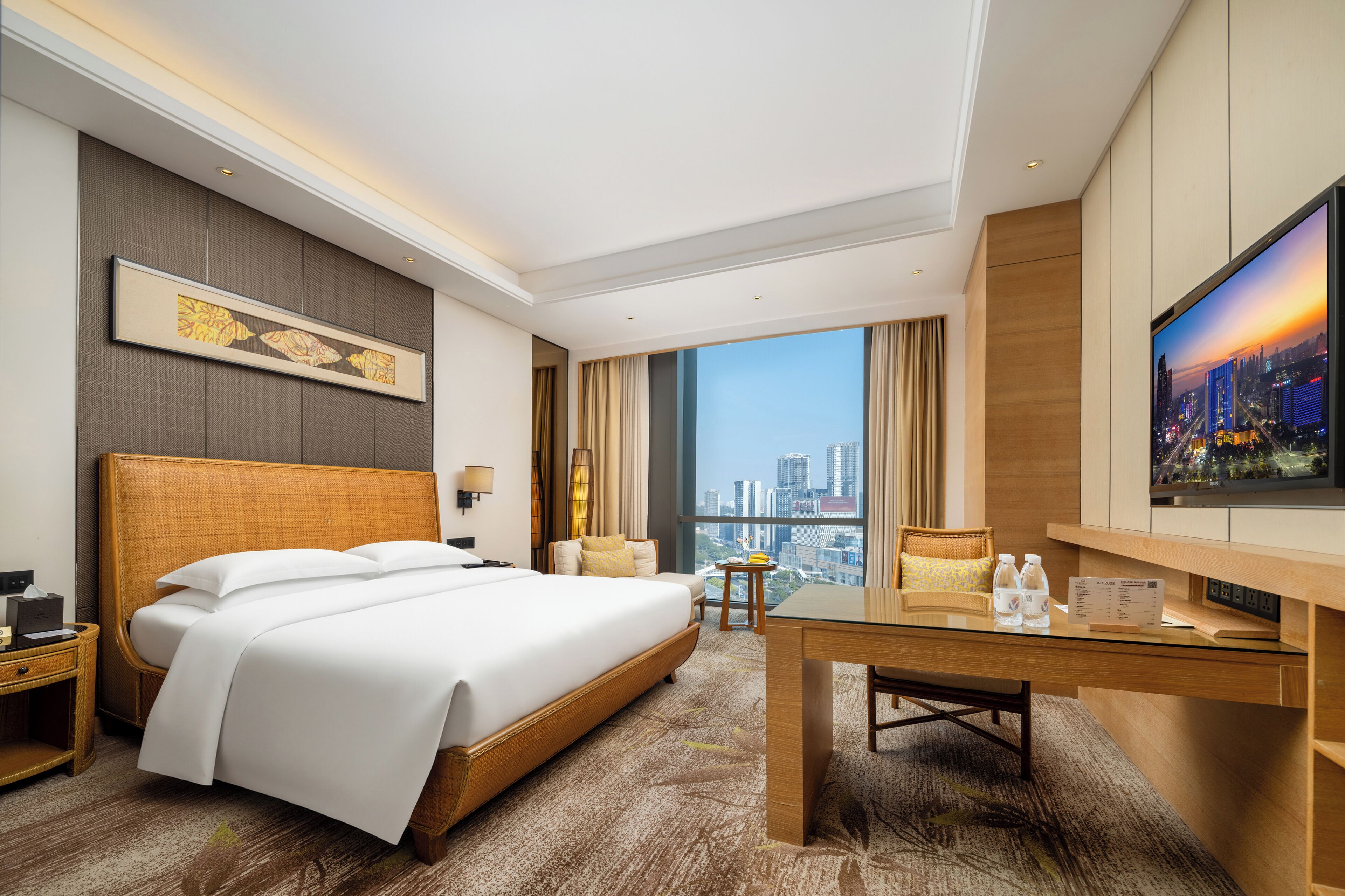 Habitación de hotel moderna con una cama grande, un escritorio, un televisor y vistas a la ciudad.