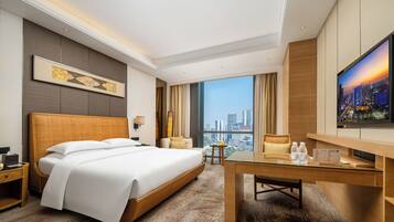 A modern hotel room with a large bed, a desk, a TV, and a city view.