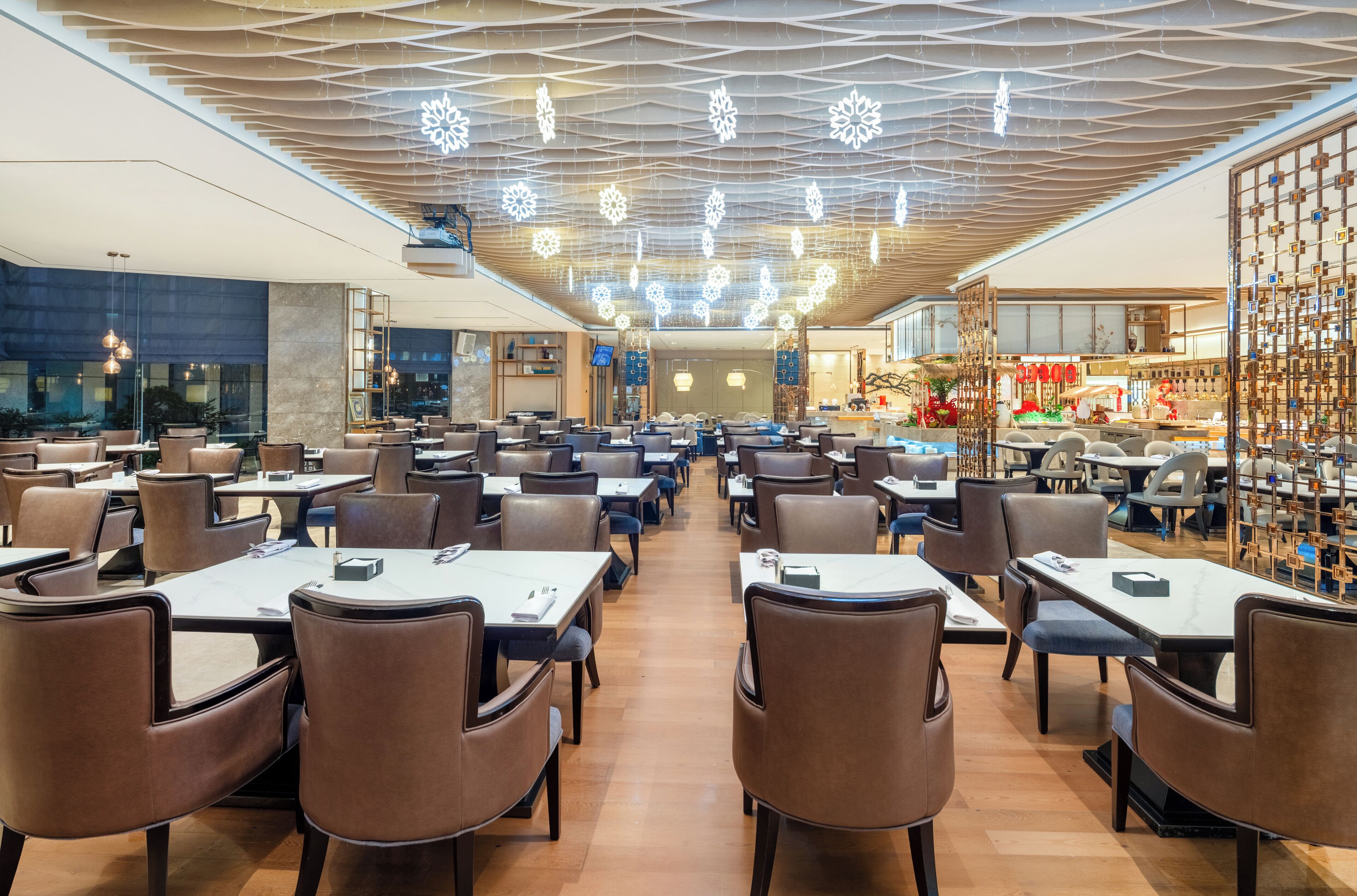 A spacious restaurant with multiple dining tables and chairs, a modern ceiling design, and a decorative wall on the right.