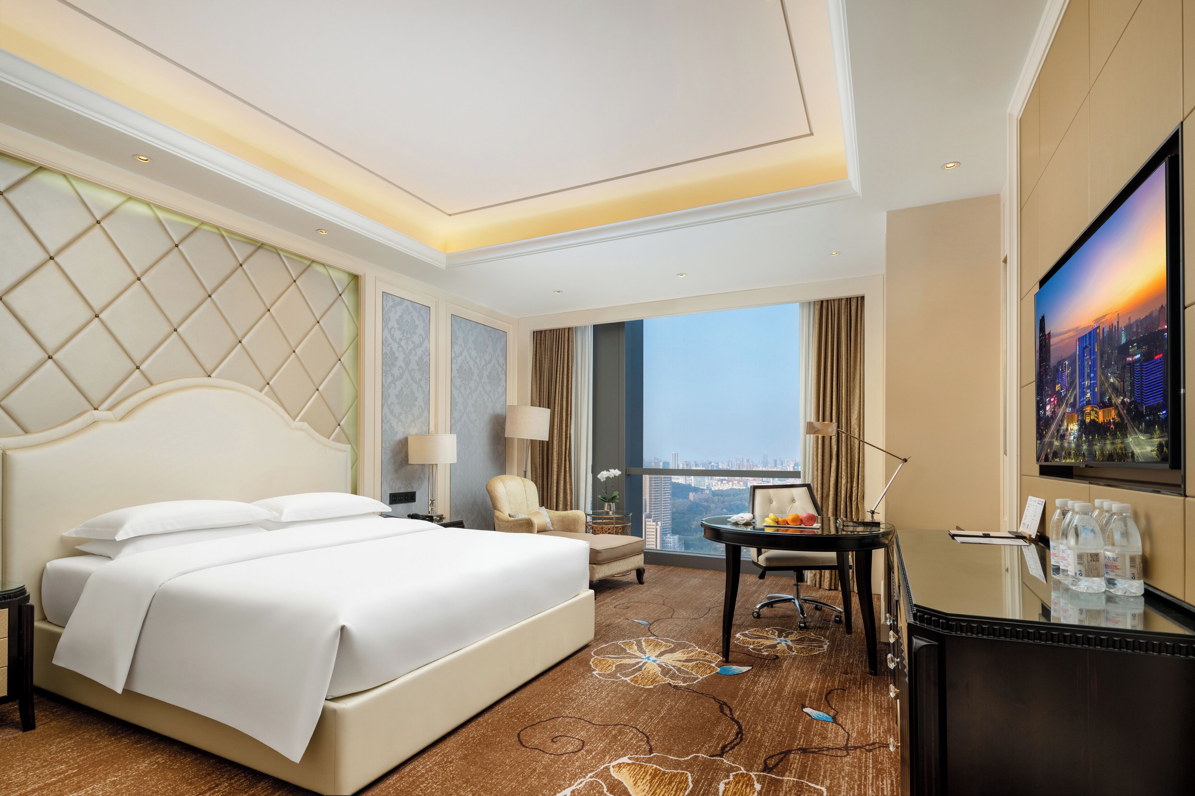 Ein Hotelzimmer mit einem großen Bett, einem Schreibtisch, einem Sessel, einem Fernseher und Blick auf die Stadt.