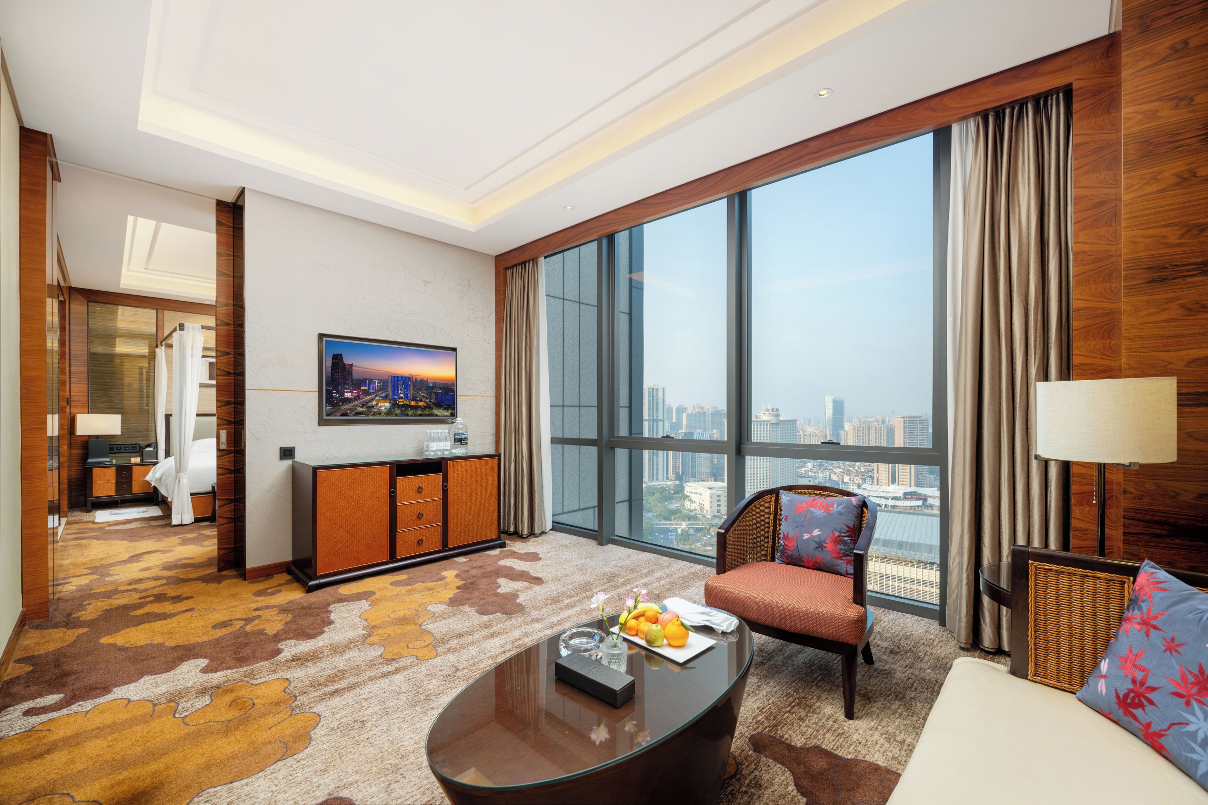 A spacious hotel room with a large window offering a city view, a comfortable seating area, and a small kitchenette.
