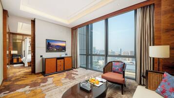 A spacious hotel room with a large window offering a city view, a comfortable seating area, and a small kitchenette.
