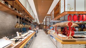 Un couloir avec un buffet sur la gauche et un stand de restauration sur la droite, agrémenté de décorations traditionnelles et doté d’un plafond en bois.