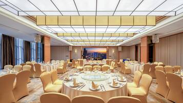 A banquet hall with round tables set for dining, large windows, and a cityscape view.