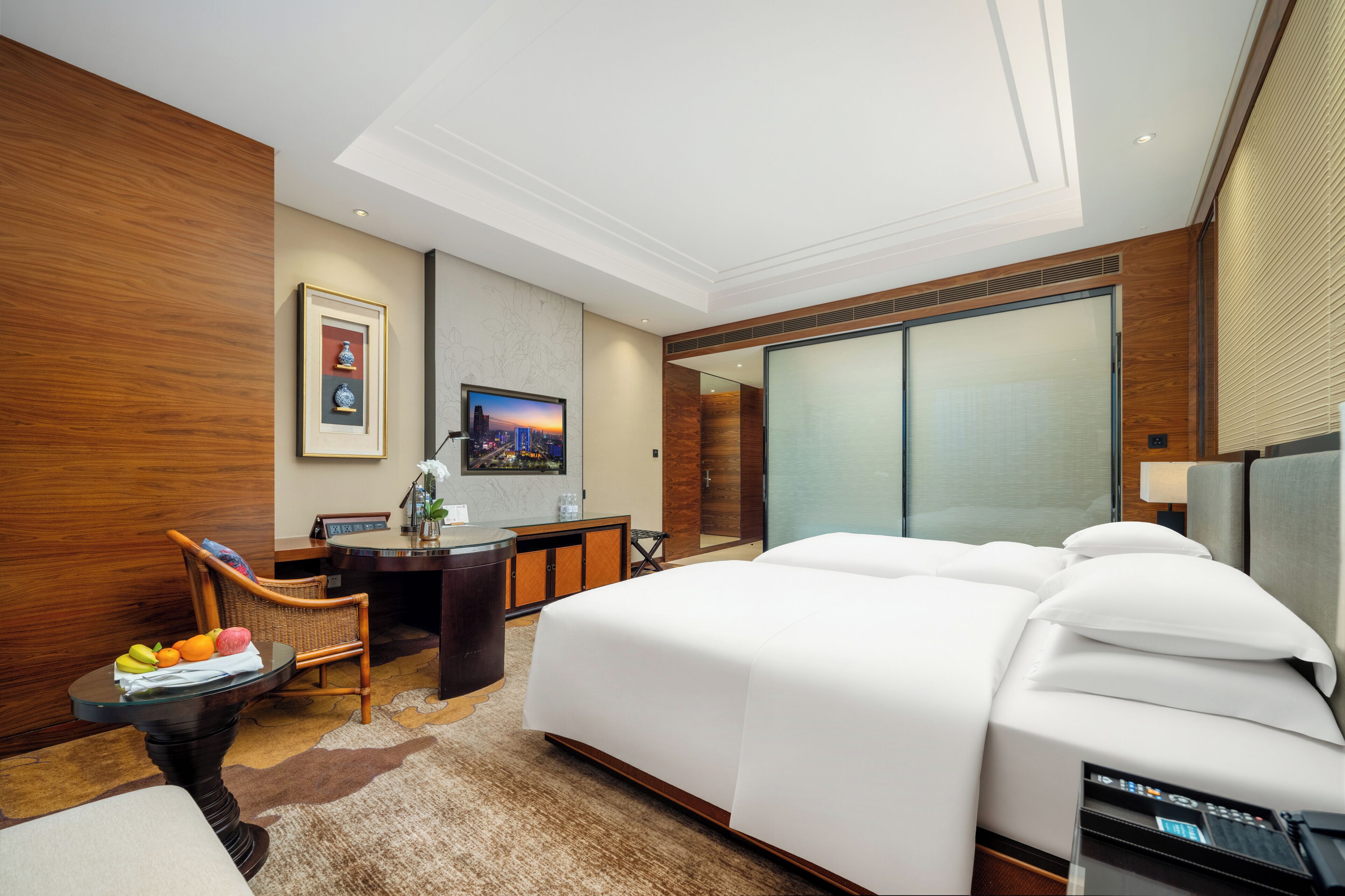 Una habitación de hotel moderna con una cama grande, un escritorio con silla, un televisor y un ventanal amplio.