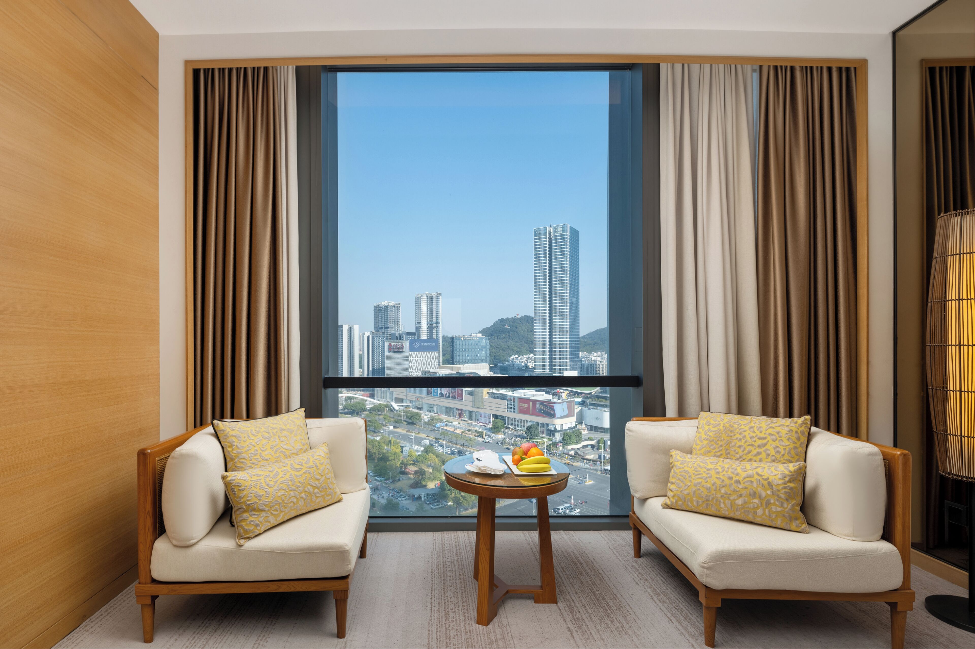 A modern hotel room with two sofas facing a large window offering a city view.