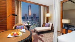 Une chambre d’hôtel avec vue sur la ville, une table à manger avec des fruits, un canapé et un téléviseur.