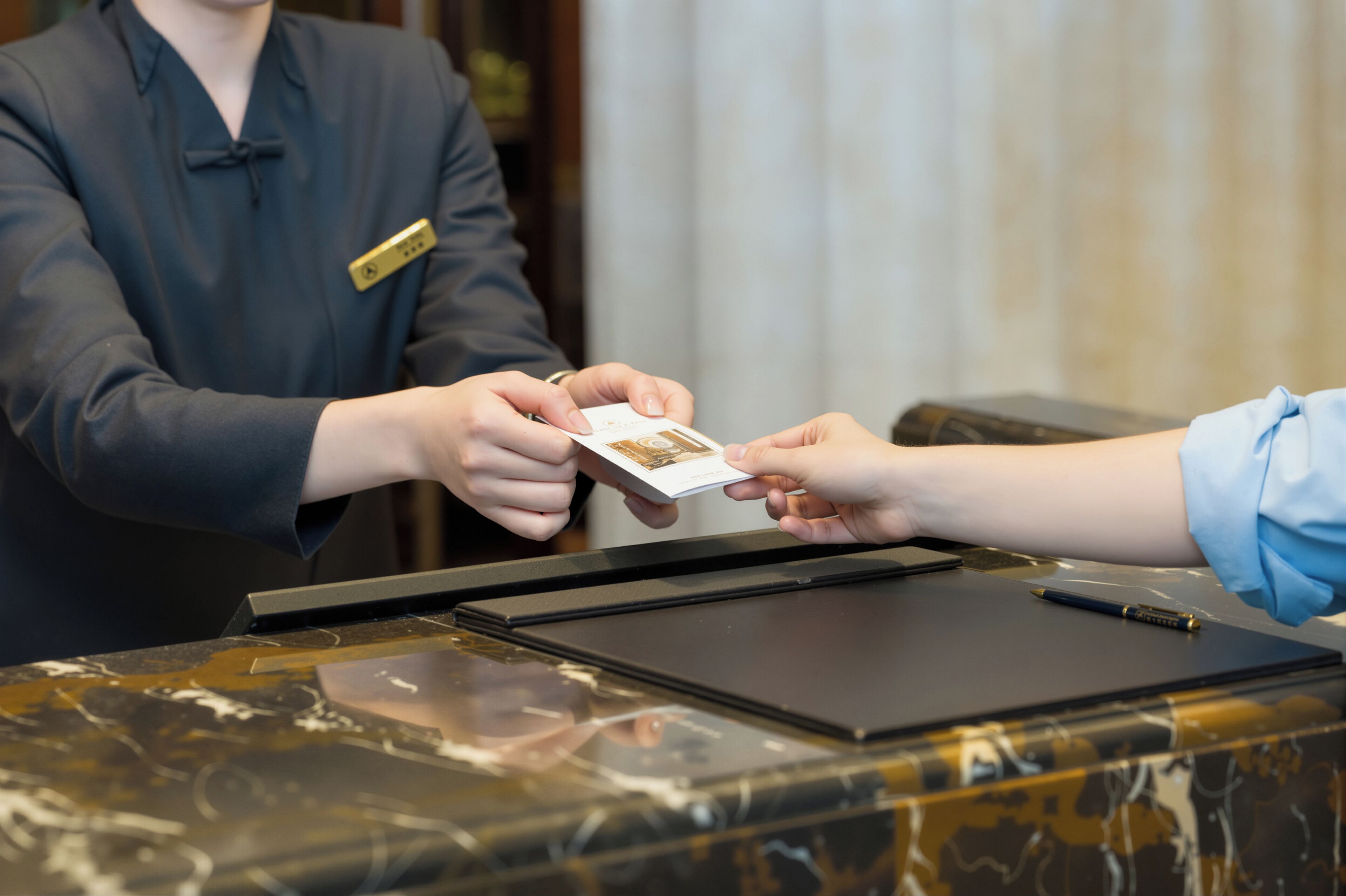 A person handing over a card to a receptionist at a reception desk.