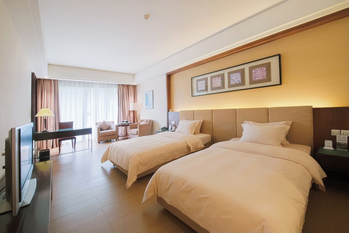 Une chambre d’hôtel avec deux lits, un bureau, une chaise et un téléviseur.