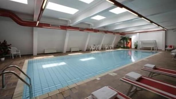 Une piscine intérieure avec un revêtement de sol carrelé, un bord de piscine rouge et blanc, et des chaises longues disposées le long du bord.