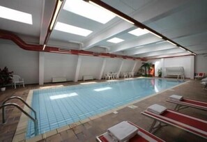 Une piscine intérieure avec un revêtement de sol carrelé, un bord de piscine rouge et blanc, et des chaises longues disposées le long du bord.