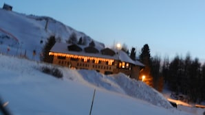 Un paysage enneigé avec un bâtiment dont les fenêtres sont illuminées et qui possède un toit en pente.