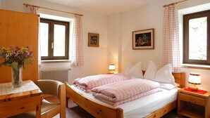 Une chambre à coucher avec un lit en bois, des tables de chevet, une chaise, un bureau, un radiateur et deux fenêtres avec des rideaux.