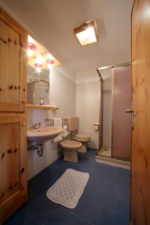 Une salle de bain avec une porte en bois, un lavabo, des toilettes et une douche.