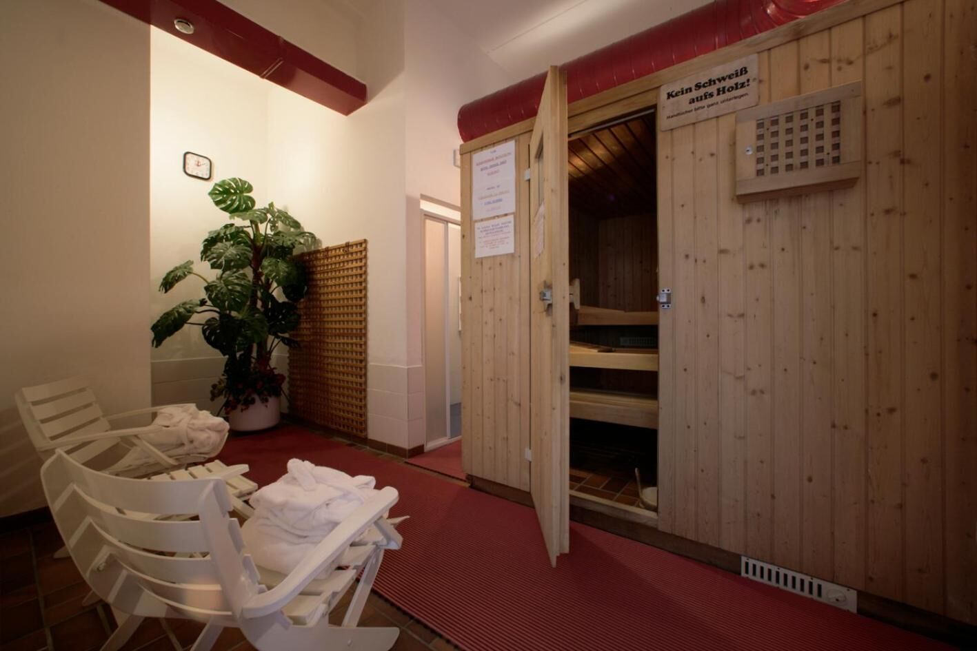 A sauna room with wooden walls, a red floor, and a bench with towels.